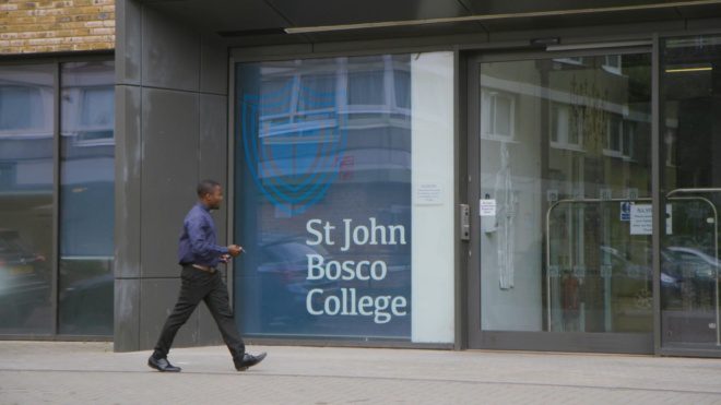 A teacher walking in front of the entrance to St John Bosco College.